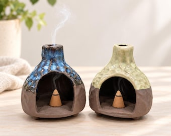 Pode incluir: Dois queimadores de incenso de cerâmica com design em forma de cúpula e uma ampla abertura frontal. Um apresenta um esmalte brilhante azul e castanho escuro, enquanto o outro tem um acabamento em verde claro e castanho escuro.