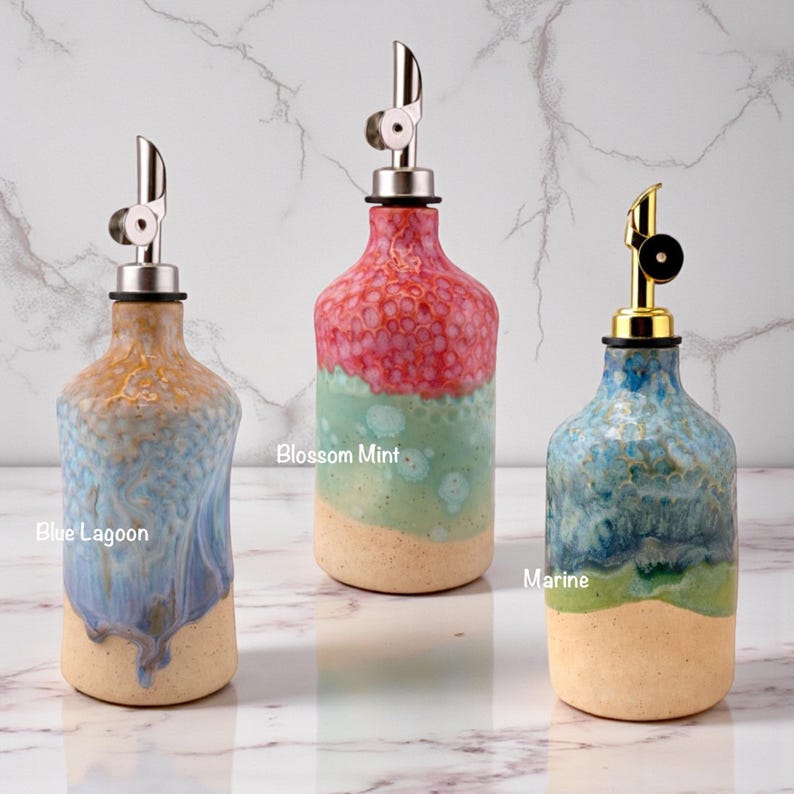 Puede incluir: Tres dispensadores de aceite de cer&aacute;mica con vertedores de metal. La botella de la izquierda es Blue Lagoon con esmalte azul y beige. La central es Blossom Mint con esmalte rosa y verde. La de la derecha es Marine con esmalte azul y verde.