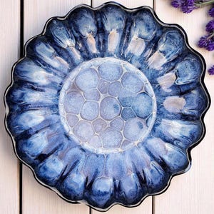 Peut inclure: Une assiette décorative en céramique avec un bord festonné, présentant un motif marbré bleu et blanc. Le centre présente un motif texturé en forme de bulles. Une pièce unique pour la décoration intérieure.