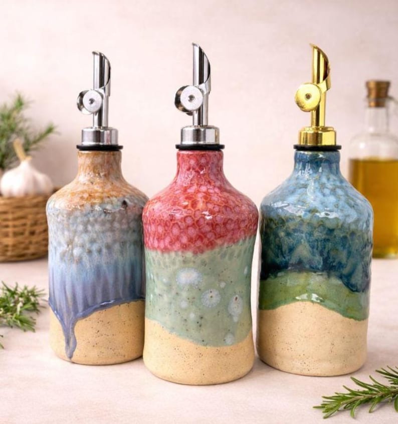 Puede incluir: Tres dispensadores de aceite de cer&aacute;mica con acabados de esmalte texturizado y multicolor. La botella de la izquierda presenta tonos azules y bronceados, la central es roja y verde, y la de la derecha es azul y verde.