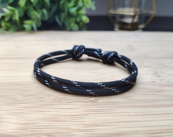 Può includere: Un braccialetto in paracord nero e bianco con un semplice design a nodo.