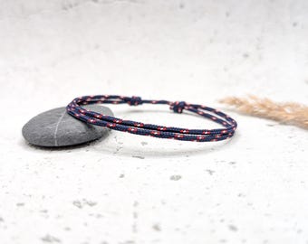 Può includere: Un braccialetto intrecciato blu navy e rosso con una semplice chiusura a nodo.