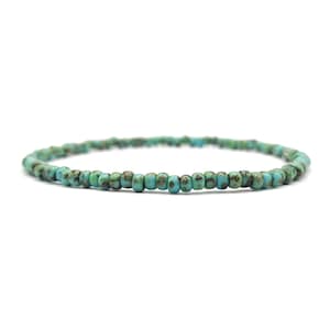 Op de afbeelding: Een turquoise blauwe kralen armband met een simpel ontwerp. De kralen zijn klein en rond en zijn geregen aan een dun koord.