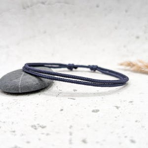 Könnte beinhalten: Ein dunkelblaues geflochtenes Armband aus Kordel mit einem einfachen Knotenverschluss.