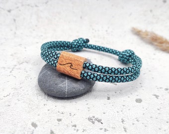Könnte beinhalten: Ein blaues und schwarzes Seil-Armband mit einem Holzperlen-Anhänger mit Wellenmuster.