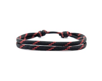 Può includere: Un braccialetto in paracord nero e rosso con un design a nodo doppio.