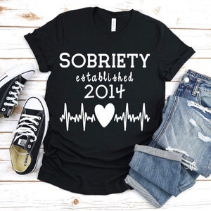 May include: Black t-shirt with white text that reads "SOBRIETY established 2014" and a white heart beat graphic.