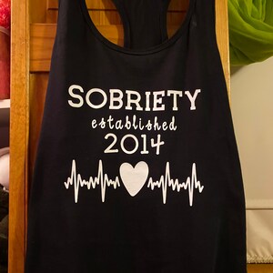 May include: Black tank top with white text that reads "SOBRIETY established 2014" with a white heart and heartbeat graphic.