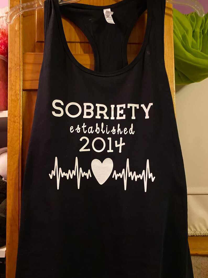 May include: Black tank top with white text that reads "SOBRIETY established 2014" with a white heart and heartbeat graphic.