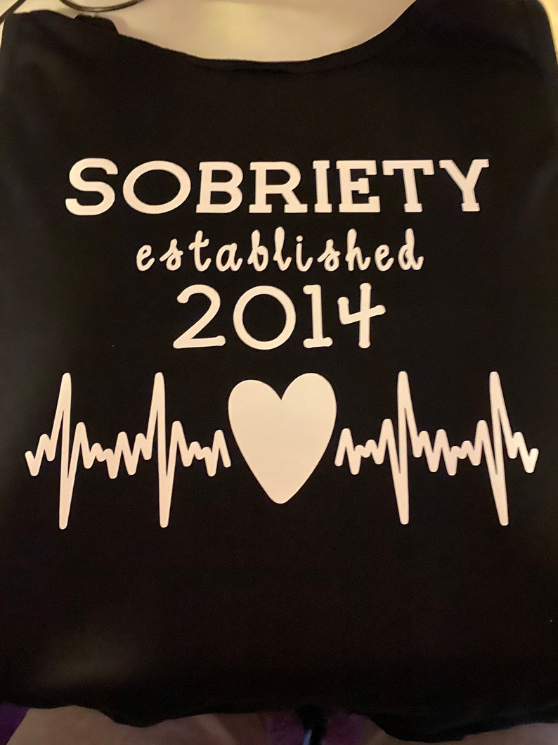 May include: Black t-shirt with white text that reads "SOBRIETY established 2014" and a white heart with a heartbeat graphic.