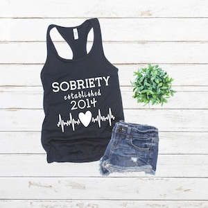 May include: Black tank top with white text that reads "SOBRIETY established 2014" with a heart and a heartbeat graphic.
