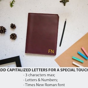 May include: A burgundy leather journal with gold lettering that says "FN" on the front. The journal is on a brown surface with a black pen and colorful chalk sticks.