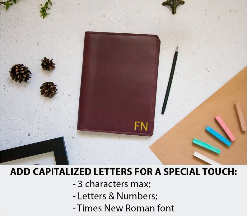 May include: A burgundy leather journal with gold lettering that says "FN" on the front. The journal is on a brown surface with a black pen and colorful chalk sticks.