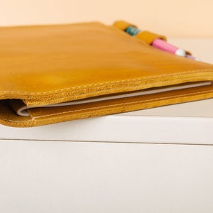 May include: A yellow leather bound notebook with a pen holder and two pens sticking out.