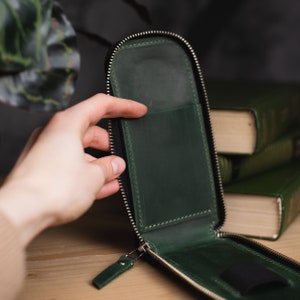 Może przedstawiać: Zielona sk&oacute;rzana kosmetyczka z zamkiem błyskawicznym i przezroczystą kieszenią z tworzywa sztucznego w środku. Kosmetyczka jest otwarta, a zamek błyskawiczny jest rozpięty.