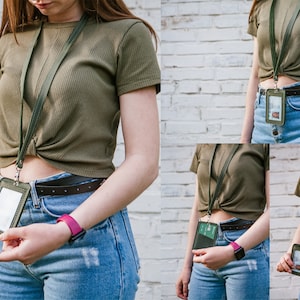 May include: A person wearing a green shirt and blue jeans with a black belt and a lanyard with a clear plastic ID card holder. The lanyard is green and has a silver clip.