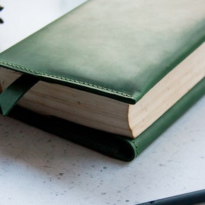 May include: A dark green leather book cover with a bookmark. The cover has a subtle gradient and is stitched around the edges.