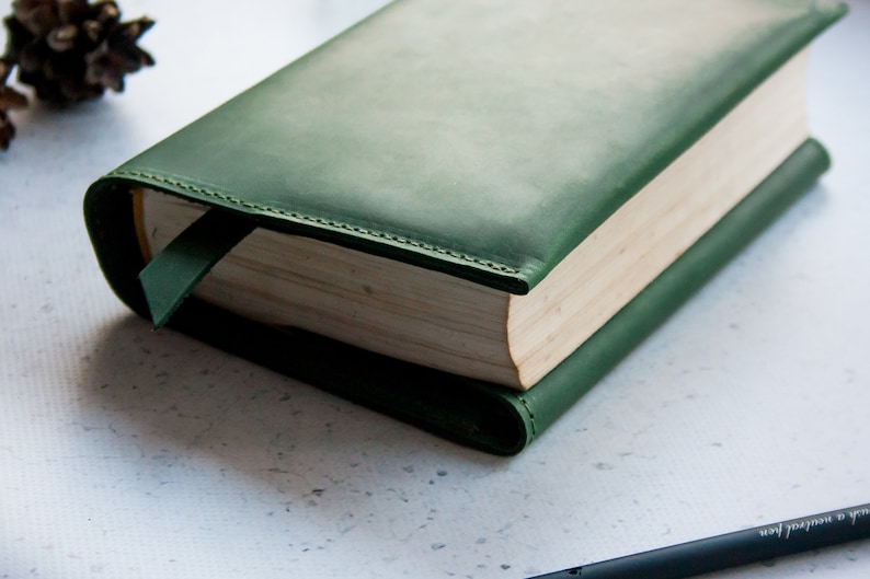 May include: A dark green leather book cover with a bookmark. The cover has a subtle gradient and is stitched around the edges.