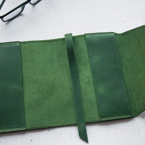 May include: A green leather book cover with a strap closure. The cover is open to reveal the inside, which is also lined with green leather.