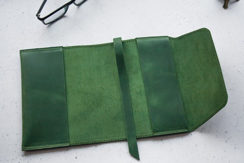 May include: A green leather book cover with a strap closure. The cover is open to reveal the inside, which is also lined with green leather.