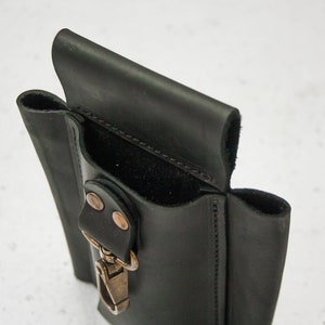 K&ouml;nnte beinhalten: Ein schwarzer Leder-Werkzeughalter mit einer einzigen Tasche und einem Metallclip. Der Halter hat eine Klappe, die &uuml;ber die Tasche geklappt wird.