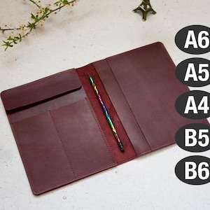 May include: Burgundy leather notebook cover with a pen holder and three pockets. The cover is open to show the inside. The cover is labeled with the sizes A6, A5, A4, B5, and B6.