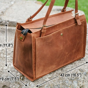 May include: A brown leather tote bag with a rectangular shape. The bag has two handles and a front pocket. Dimensions are 42 cm long, 30 cm high, and 19 cm wide. The bag has a zipper closure and brass-colored hardware.
