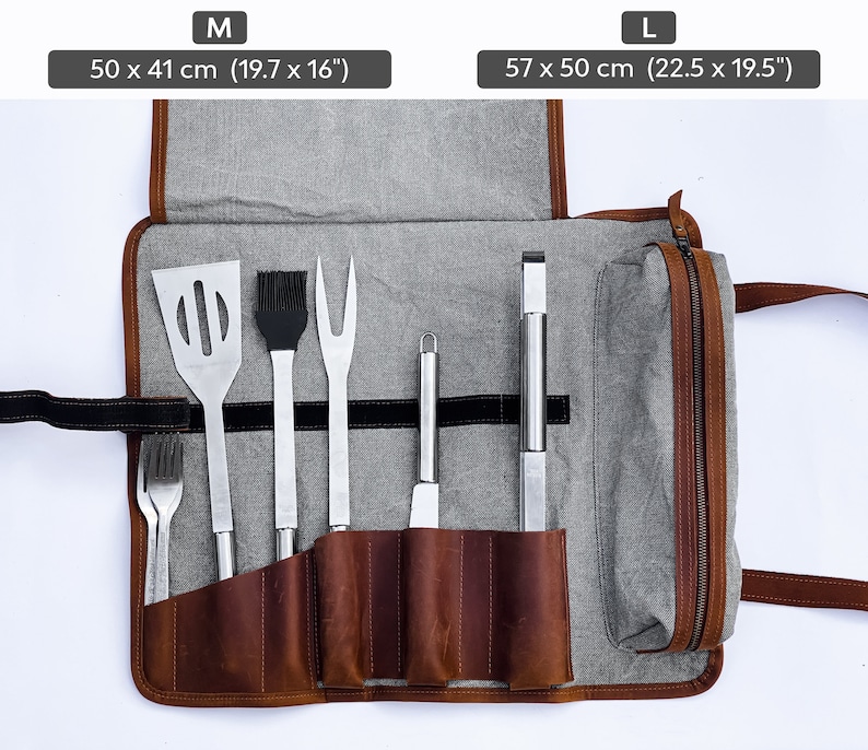 May include: A brown leather grilling tool roll with a gray canvas exterior. The roll is unrolled and shows six metal grilling tools, including a spatula, a basting brush, a fork, a knife, a pair of tongs, and a small tool. The roll has a zipper closure and a carrying handle. The roll is available in two sizes: M (50 x 41 cm or 19.7 x 16 inches) and L (57 x 50 cm or 22.5 x 19.5 inches).