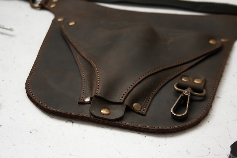 Pode incluir: Um cinto de couro castanho com uma bolsa grande anexada. A bolsa tem uma aba com fecho de press&atilde;o e um gancho de metal. O cinto &eacute; costurado com fio castanho.