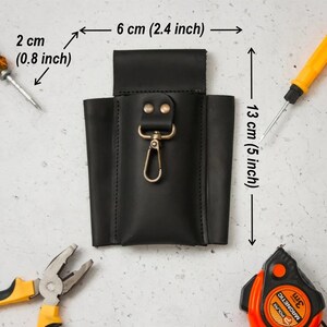 K&ouml;nnte beinhalten: Schwarzer Leder-Werkzeughalter mit einem Metallclip und zwei Druckkn&ouml;pfen. Der Halter ist 6 cm breit und 13 cm hoch.