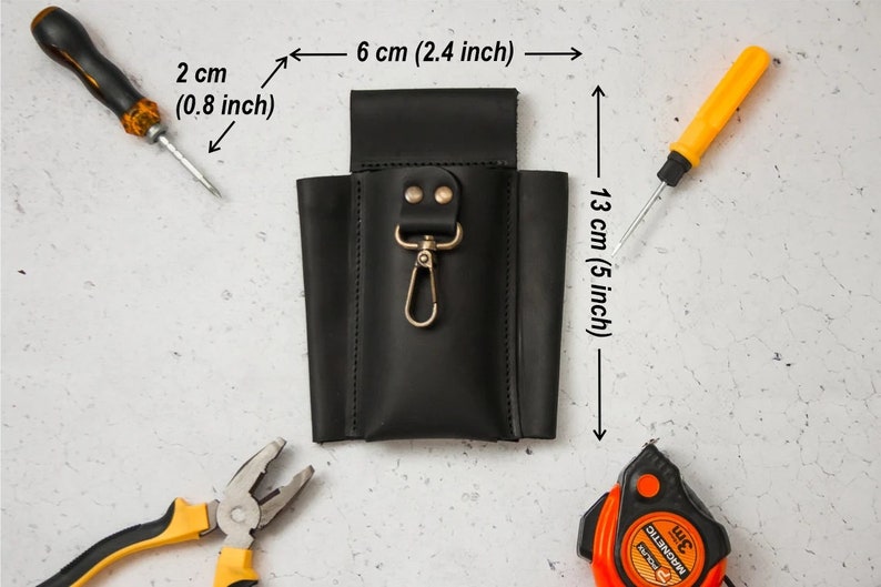 K&ouml;nnte beinhalten: Schwarzer Leder-Werkzeughalter mit einem Metallclip und zwei Druckkn&ouml;pfen. Der Halter ist 6 cm breit und 13 cm hoch.