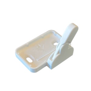 May include: A white 3D-printed phone case with a hinged clip. The case has a rectangular base with rounded corners and two circular holes. The clip is attached to the side and can be opened and closed.