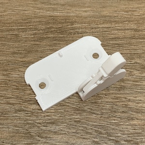 May include: White plastic 3D printed part with a lever and two holes. The part is designed to be attached to a larger object.