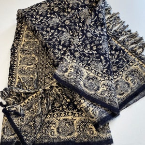 Puede incluir: Un chal plegado azul marino y crema con un estampado floral y cachemir. El chal tiene un borde con flecos y un dise&ntilde;o de borde detallado. La tela parece suave y texturizada, ideal para abrigo y estilo.