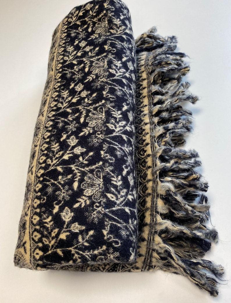 Puede incluir: Bufanda enrollada azul marino con un estampado floral crema y bordes con flecos. La bufanda presenta un dise&ntilde;o bot&aacute;nico detallado a lo largo de los bordes y en toda la tela. Los bordes con flecos a&ntilde;aden un toque decorativo a este accesorio.