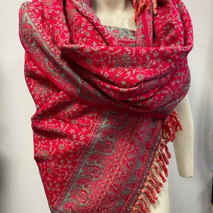 Peut inclure: Un châle à motifs roses et verts avec des franges. Le châle est drapé sur un mannequin.