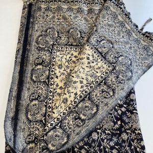Puede incluir: Textil plegado con dise&ntilde;os florales y cachemir en azul marino y crema. La tela presenta patrones intrincados y un borde con flecos. Probablemente sea un chal, una manta o un pa&ntilde;o decorativo.