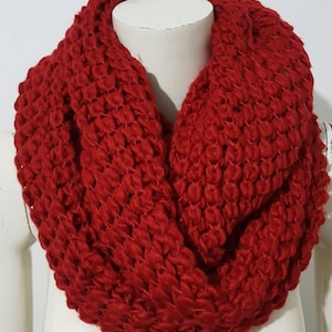May include: A red knitted infinity scarf. The scarf is made of a soft, chunky yarn and has a loose, drapey texture.