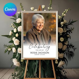 May include: A framed memorial portrait of a woman, displayed on an easel, surrounded by white roses and greenery. The portrait has the text "Celebrating The Life Of Rosie Jackson 26.08.1950 - 20.12.2025". A Canva logo is in the upper left corner.