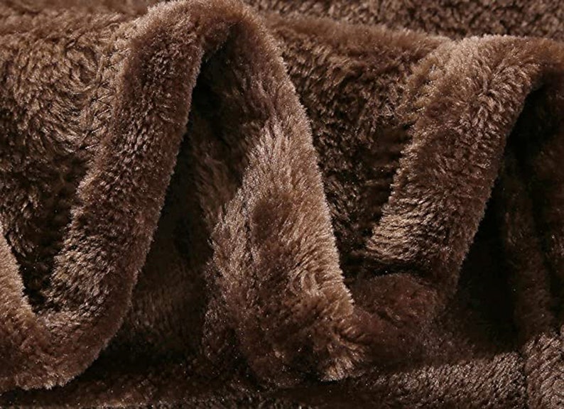 May include: Close-up of a brown plush fabric with a soft, fuzzy texture. The fabric is folded in a way that shows the depth and texture of the material.