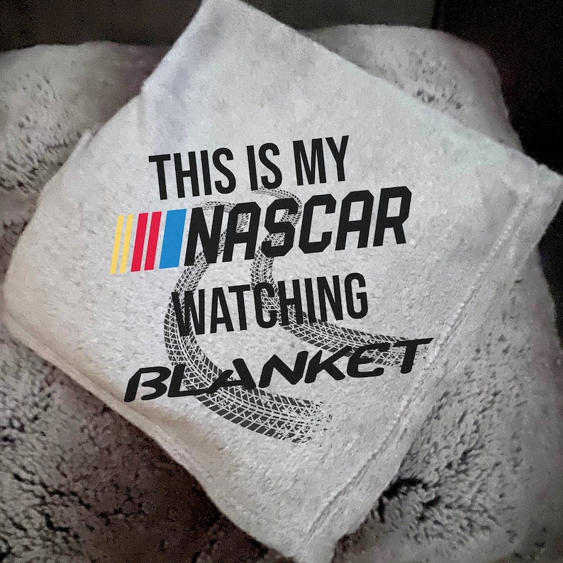May include: A grey blanket with the text "This is my NASCAR watching blanket" printed on it. The text is in black and the blanket has a tyre track design.