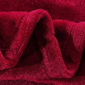 May include: Close-up of a soft, plush burgundy red blanket. The fabric is fuzzy and has a textured surface.