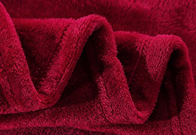 May include: Close-up of a soft, plush burgundy red blanket. The fabric is fuzzy and has a textured surface.