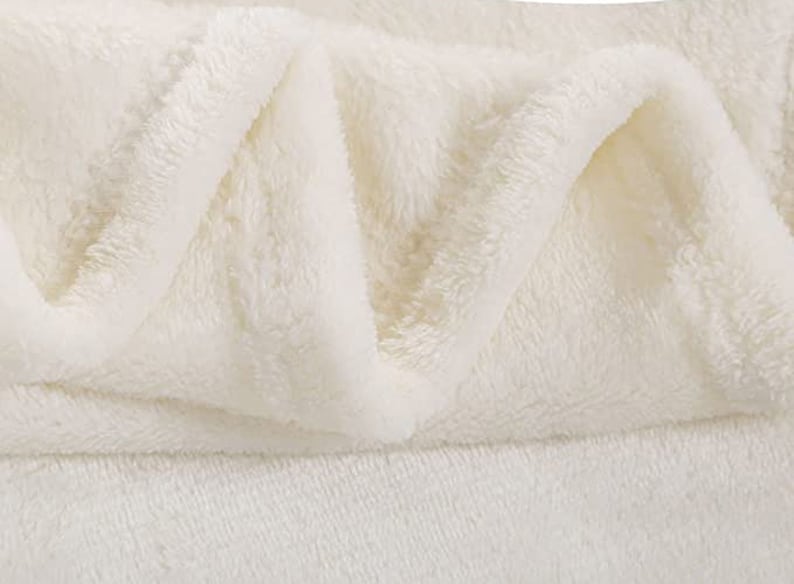 May include: A close-up of a white plush blanket folded to show its soft, fluffy texture.