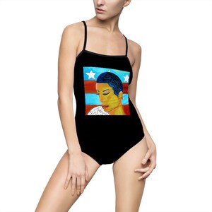 May include: Black swimsuit with a graphic print of a woman's face with blue hair against a red, white and blue background. The background resembles the American flag.