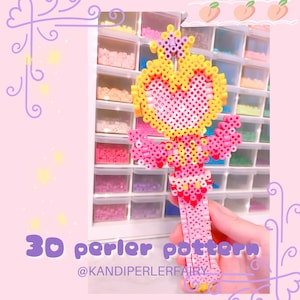 Pode incluir: Um padrão de contas perler 3D para uma varinha rosa e amarela com um design em forma de coração. O padrão é etiquetado como "3D perler pattern" e "@KANDIPERLERFAIRY".