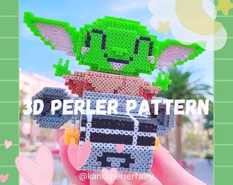 Puede incluir: Un patrón de cuentas Perler en 3D de un personaje verde de Baby Yoda sentado en una nave espacial de cuentas Perler gris y negra. El patrón se titula "3D Perler Pattern" e incluye el nombre de usuario de las redes sociales "@kandiperlerfairy".