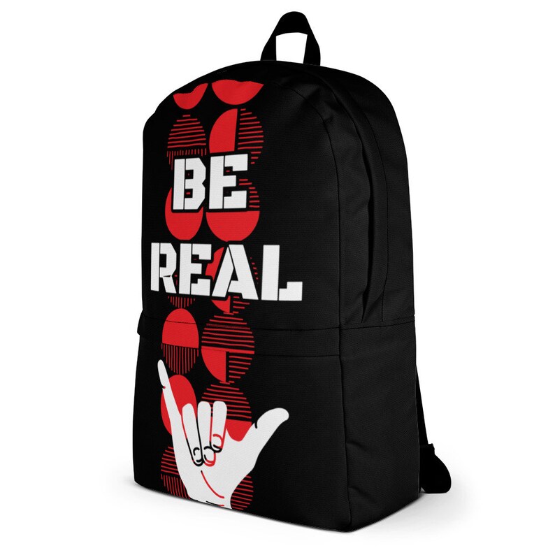 May include: Black backpack with the words "BE REAL" in white block letters. The backpack features a red and white graphic design and a white hand making a shaka sign.