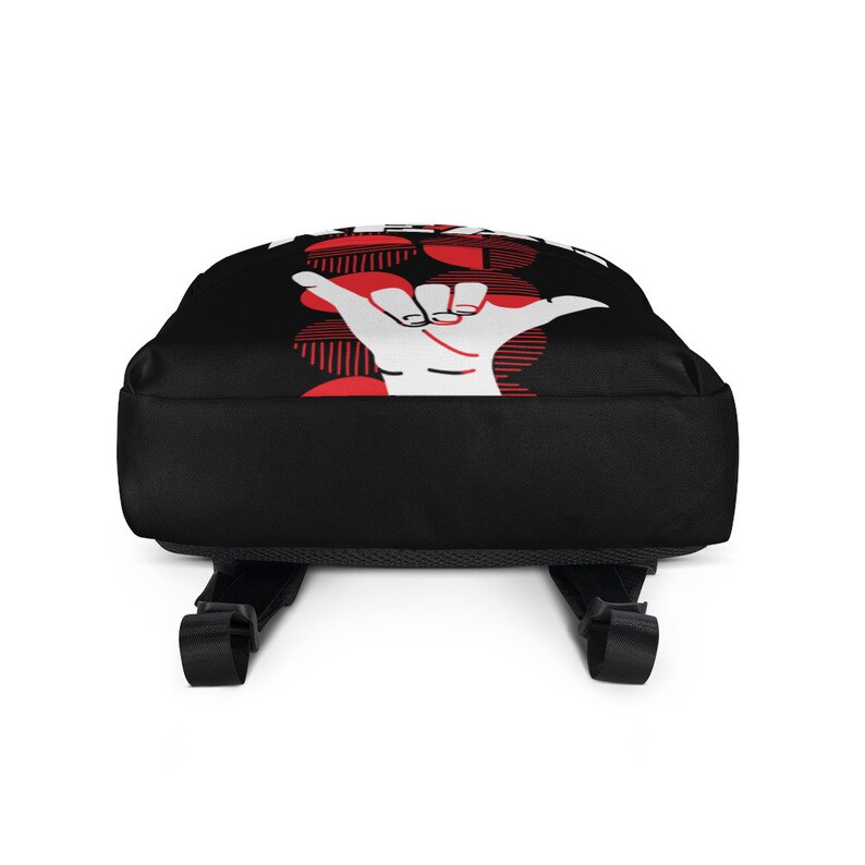 May include: Black backpack with a white hand gesture graphic and red accents. The design includes a red circular pattern with vertical lines. Adjustable black shoulder straps and a top handle are visible.