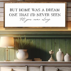 May include: A framed wooden sign with the text "BUT HOME WAS A DREAM ONE THAT I'D NEVER SEEN Til you came along." The sign is above a white dresser with multiple drawers. A lamp, vase, and decorative items are on the dresser. The bottom of the image reads "FULLY CUSTOMIZABLE - SIZES, COLORS, FONTS."